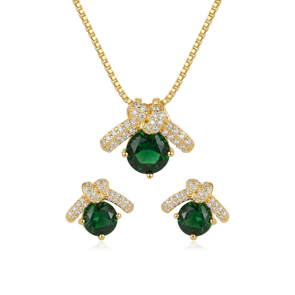Conjunto de semijoia dourada com colar e par de brincos, ambos com pingente em formato de laço cravejado de zircônias e uma pedra central oval verde esmeralda, dentro de uma caixa branca.