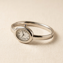 Relógio bracelete oval prata em aço inox com mostrador analógico e algarismos romanos.