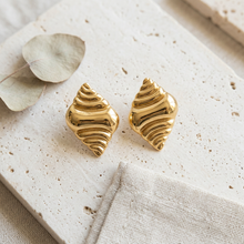 Brinco Maré Dourado em aço inoxidável com design de ondas.