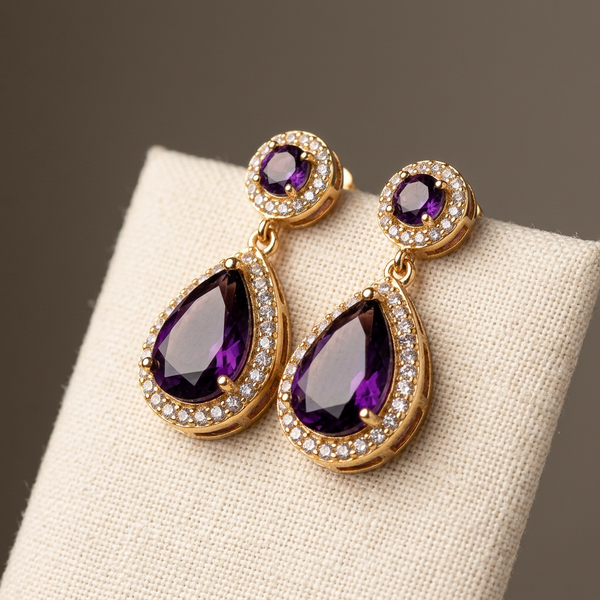 Brinco gota violeta dourado com cristais em fundo espelhado.