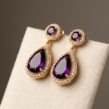 Brinco gota violeta dourado com cristais em fundo espelhado.