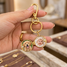 Chaveiro relicário redondo dourado com fotos de um cachorro e um bebê.