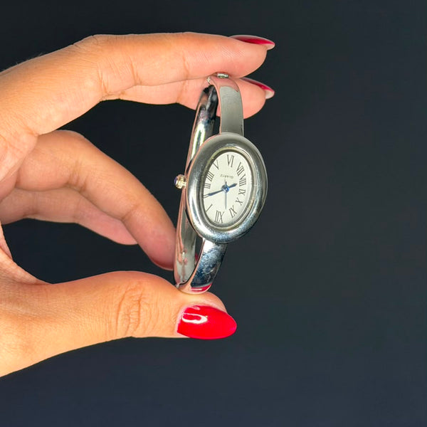 Relógio bracelete oval prata em aço inox com mostrador analógico e algarismos romanos.