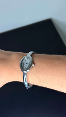Relógio bracelete oval prata em aço inox com mostrador analógico e algarismos romanos.
