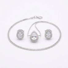 Conjunto de colar e brincos prateados com pingente e brincos em formato de gota, com uma pedra cristal central e um halo de pedras menores, sobre um mostruário bege.