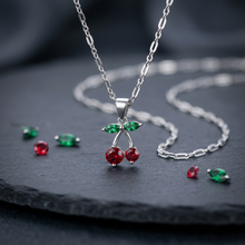 Colar com pingente de cereja em prata e detalhes vermelhos e verdes.