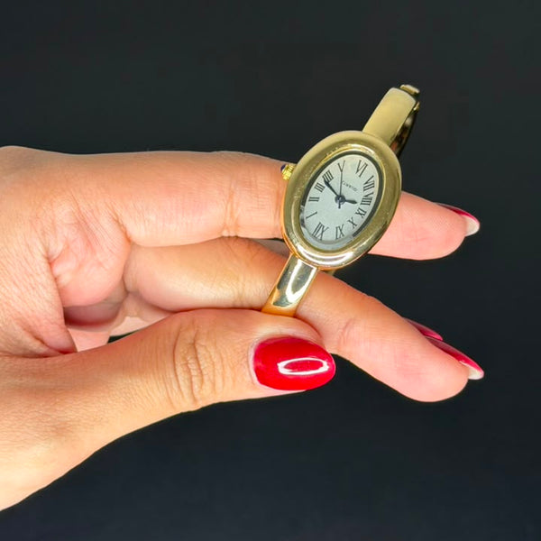 Relógio bracelete oval dourado com mostrador branco e números romanos.