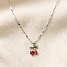 Colar com pingente de cereja em prata e detalhes vermelhos e verdes.